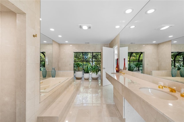 bathroom with double vanity, recessed lighting, a tub with jets, tile walls, and a sink