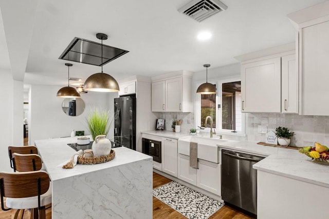 kitchen featuring visible vents, black appliances, light wood-style flooring, a sink, and decorative backsplash