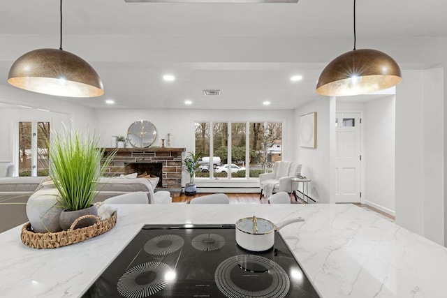 kitchen with a fireplace with raised hearth, light stone counters, decorative light fixtures, wood finished floors, and recessed lighting