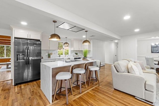 kitchen with light wood finished floors, a kitchen island, stainless steel fridge with ice dispenser, a kitchen bar, and light countertops