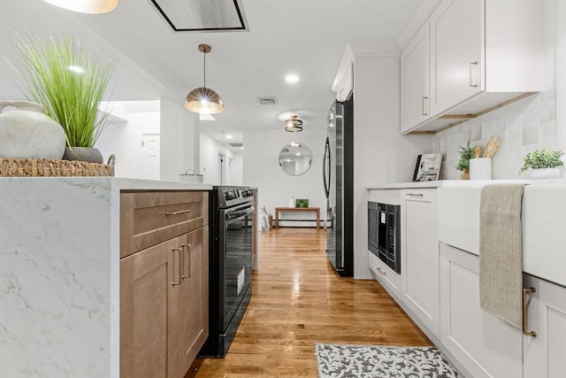 kitchen featuring light wood finished floors, hanging light fixtures, black appliances, white cabinets, and tasteful backsplash