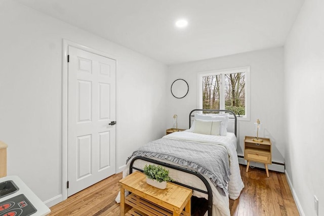 bedroom featuring a baseboard heating unit, baseboards, and light wood finished floors