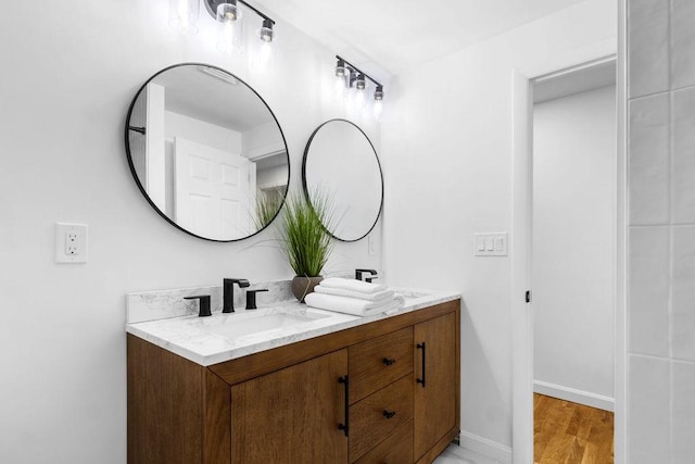 full bath with a sink, baseboards, wood finished floors, and double vanity