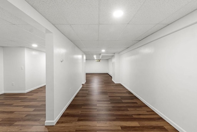 hall featuring a drop ceiling, baseboards, and dark wood-type flooring