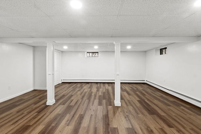 finished basement with a paneled ceiling, wood finished floors, baseboards, and a baseboard radiator