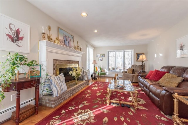 living area with baseboard heating, recessed lighting, a glass covered fireplace, and wood finished floors