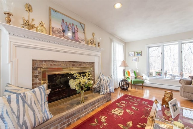 living area featuring a baseboard radiator, a brick fireplace, and wood finished floors