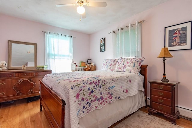 bedroom with a baseboard heating unit, wood finished floors, and a ceiling fan