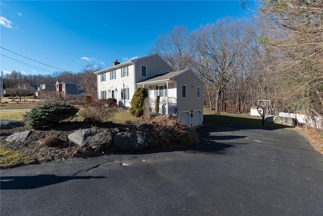 view of side of property featuring aphalt driveway, a garage, and a chimney