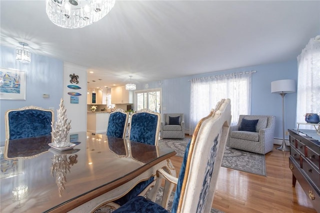 dining room with light wood finished floors, baseboard heating, and an inviting chandelier