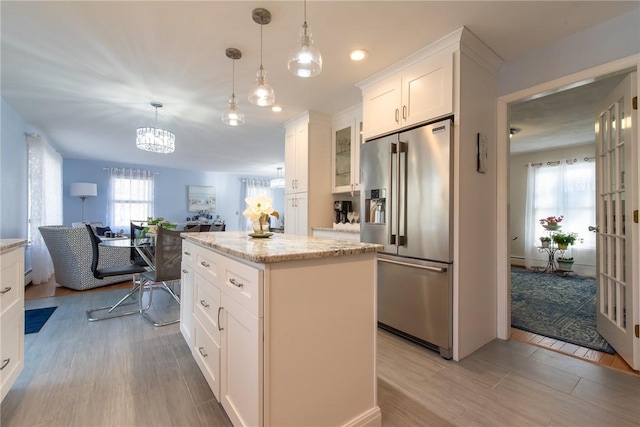 kitchen featuring light stone countertops, a kitchen island, white cabinets, decorative light fixtures, and high quality fridge