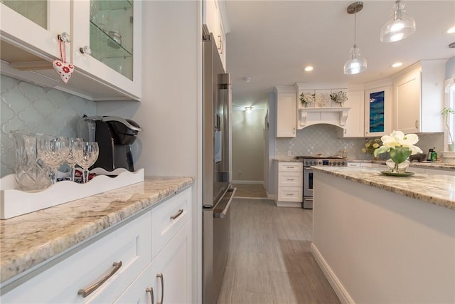 kitchen with stainless steel appliances, white cabinets, glass insert cabinets, pendant lighting, and tasteful backsplash