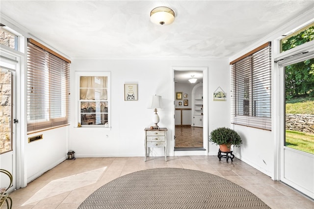 interior space featuring light tile patterned floors, baseboards, a healthy amount of sunlight, and crown molding