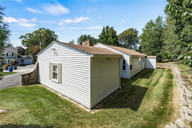 view of home's exterior featuring a lawn, roof with shingles, and a chimney