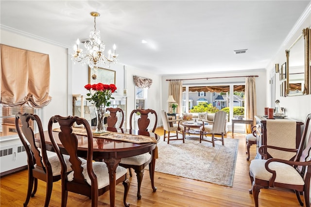 dining area with a notable chandelier, visible vents, light wood-type flooring, and ornamental molding