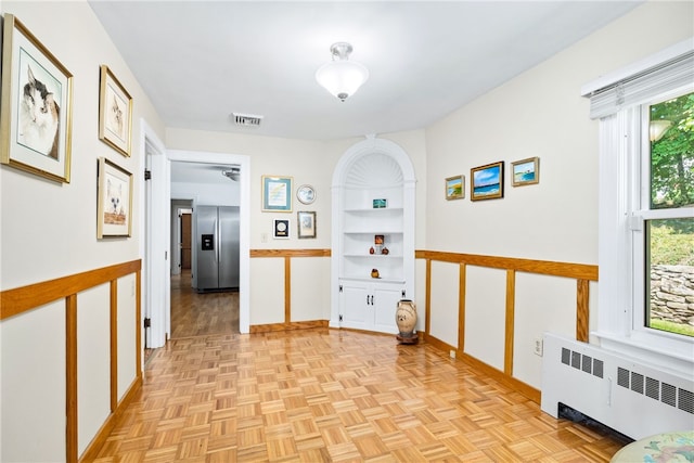 hallway with visible vents, radiator, baseboards, and built in shelves