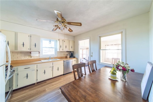 kitchen featuring light wood-type flooring, a sink, appliances with stainless steel finishes, light countertops, and decorative backsplash