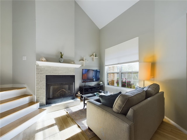 living area with a brick fireplace, wood finished floors, baseboards, and high vaulted ceiling