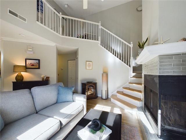 living area featuring visible vents, stairs, a fireplace, a high ceiling, and wood finished floors