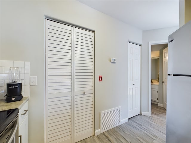 interior space featuring visible vents, baseboards, multiple closets, light wood-style flooring, and freestanding refrigerator