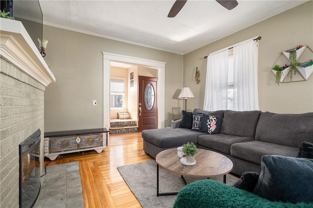 living room with crown molding, a brick fireplace, wood finished floors, and ceiling fan