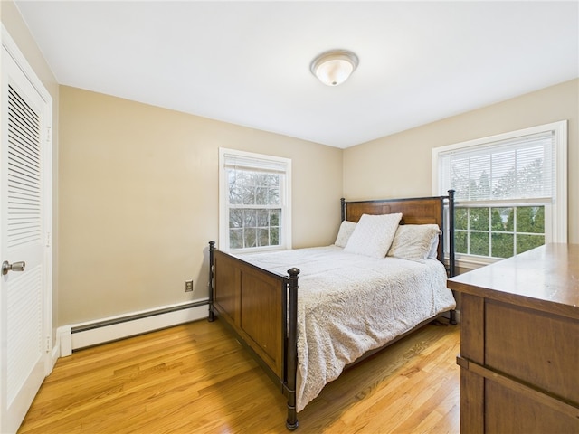 bedroom with multiple windows, light wood finished floors, and a baseboard radiator