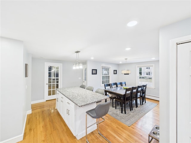 kitchen with a breakfast bar area, a chandelier, light wood-style flooring, and white cabinetry