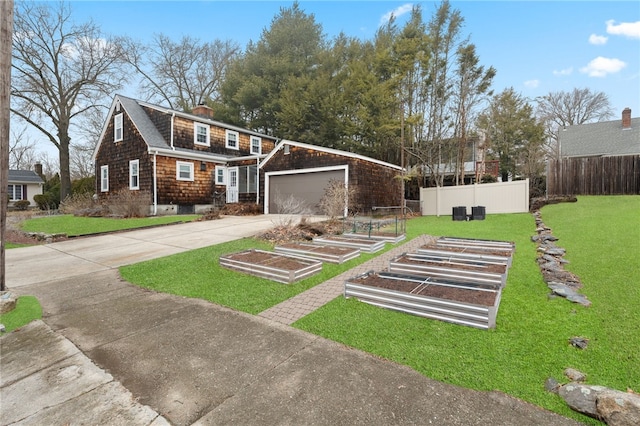 exterior space featuring a front lawn, fence, concrete driveway, a garage, and a vegetable garden