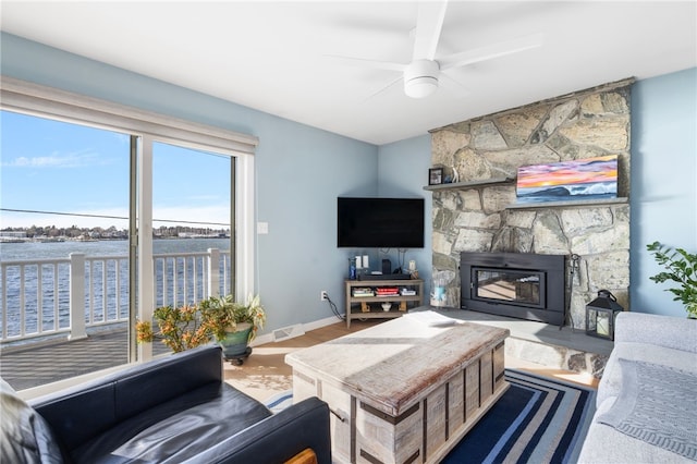 living area with wood finished floors, baseboards, a fireplace, ceiling fan, and a water view