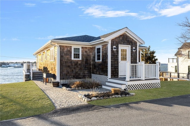 view of front of home featuring a front lawn, a water view, and a shingled roof