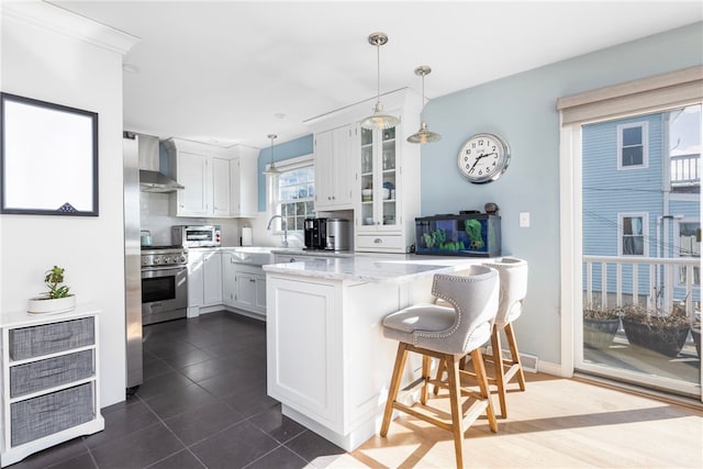 kitchen with glass insert cabinets, wall chimney range hood, light stone countertops, stainless steel range, and white cabinetry