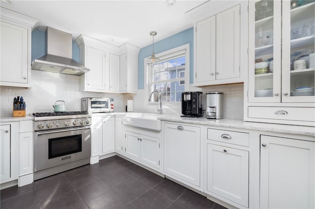 kitchen featuring high end stove, a sink, white cabinetry, wall chimney range hood, and glass insert cabinets