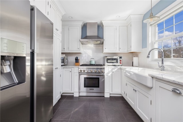 kitchen featuring backsplash, wall chimney range hood, appliances with stainless steel finishes, white cabinets, and a sink