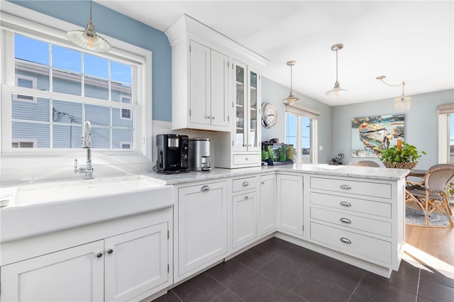 kitchen with a peninsula, a sink, glass insert cabinets, pendant lighting, and white cabinetry