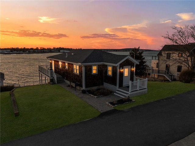 view of front of home featuring a water view, a front yard, and a shingled roof