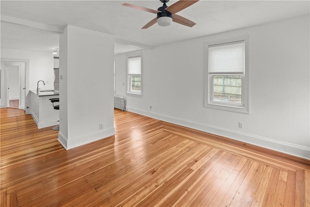 interior space featuring light wood-style flooring, a sink, radiator heating unit, baseboards, and ceiling fan