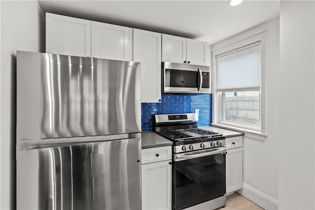 kitchen featuring decorative backsplash, white cabinets, appliances with stainless steel finishes, and baseboards