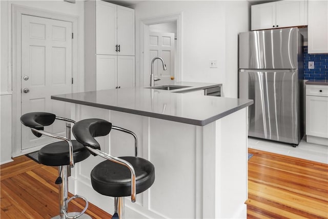 kitchen featuring a sink, white cabinetry, freestanding refrigerator, a breakfast bar area, and decorative backsplash