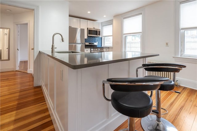 kitchen featuring tasteful backsplash, light wood-type flooring, white cabinets, stainless steel appliances, and a sink