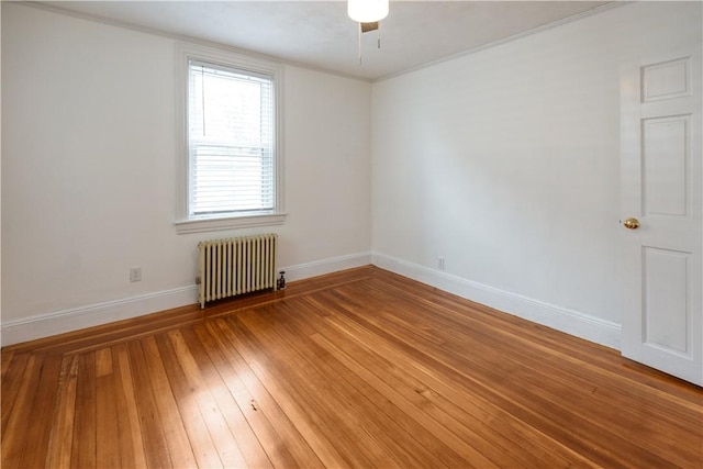 spare room featuring light wood-style floors, baseboards, radiator, and ornamental molding