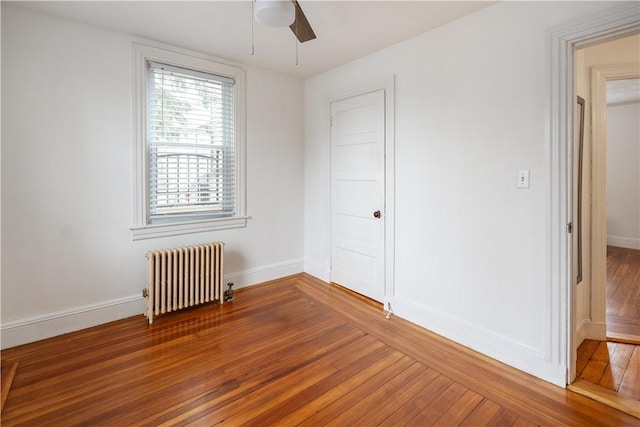 unfurnished bedroom with hardwood / wood-style flooring, radiator, a ceiling fan, and baseboards