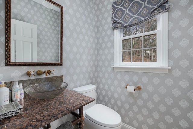 bathroom featuring toilet, wallpapered walls, and a sink