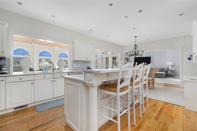 kitchen featuring wallpapered walls, white cabinets, light wood-style floors, and a sink