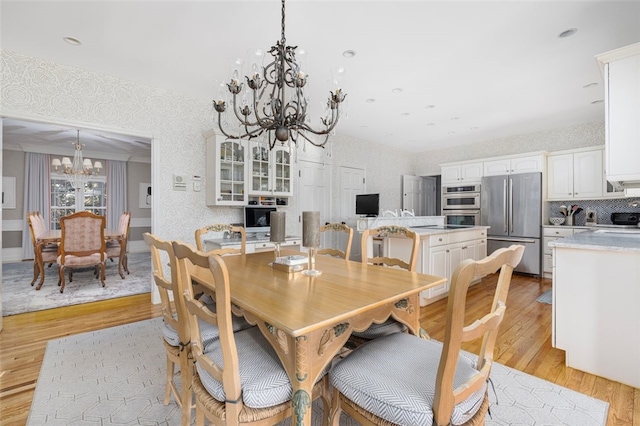 dining room with wallpapered walls, a notable chandelier, and light wood-type flooring