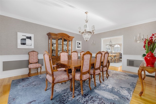 dining area with an inviting chandelier, ornamental molding, wood finished floors, and wainscoting