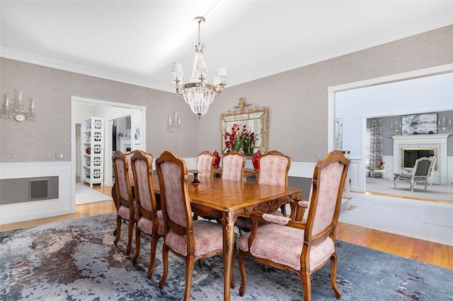 dining space featuring wood finished floors, a wainscoted wall, a fireplace, crown molding, and a notable chandelier