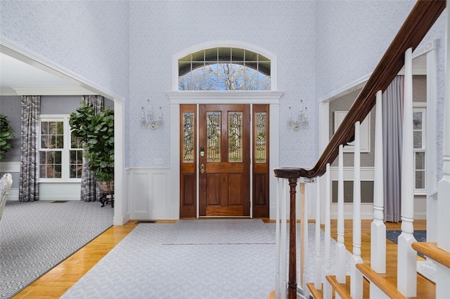 entryway featuring stairway, wood finished floors, wallpapered walls, a high ceiling, and wainscoting