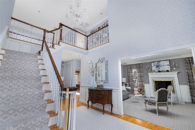 staircase featuring a notable chandelier, wallpapered walls, wood finished floors, a fireplace, and wainscoting