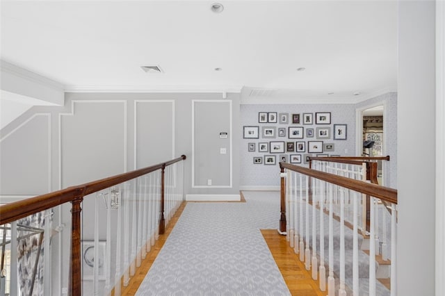 hallway with visible vents, an upstairs landing, ornamental molding, and a decorative wall