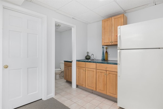 kitchen with dark countertops, light tile patterned floors, freestanding refrigerator, and a paneled ceiling